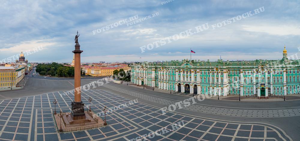 На фотографии изображена Дворцовая площадь в Санкт-Петербурге с Александровской колонной в центре. Справа расположен Зимний дворец, часть комплекса Эрмитажа, украшенный зелеными и белыми фасадами. Вдали виден купол Исаакиевского собора. Утреннее освещение придает площади спокойную и величественную атмосферу.